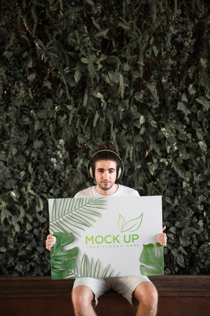 Free Man Presenting Poster Mockup In Front Of Leaves Psd