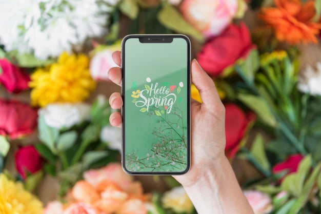 Free Hand Holding Smartphone Mockup Above Flowers Psd