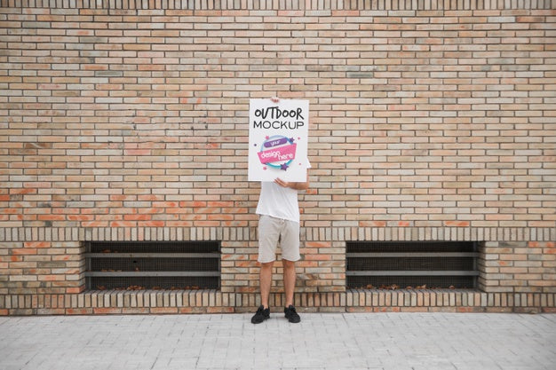 Free Man Holding Poster Mockup In Front Of Brick Wall Psd