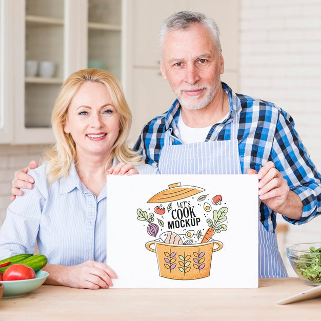 Free Senior Couple In Kitchen Holding Cardboard Mock-Up Psd
