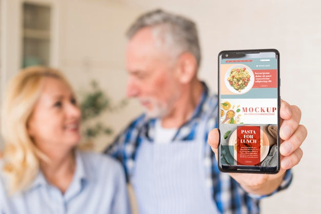 Free Senior Couple In Kitchen Holding Phone Mock-Up Psd