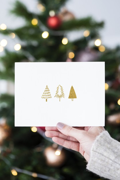Free Woman Holding A Christmas Card In Front Of A Christmas Tree Mockup Psd