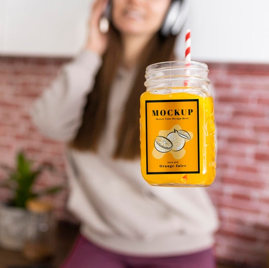 Free Woman Holding Orange Juice Jar While Listening To Music On Headphones Psd